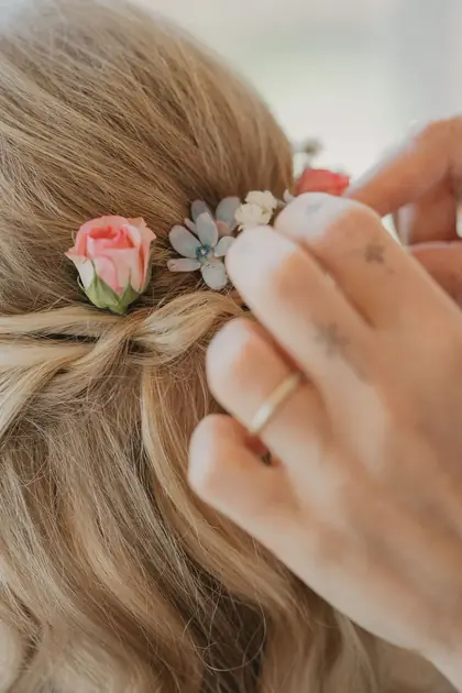 Blütenschmuck wird in die Brautfrisur gesteckt