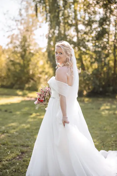 Braut mit offenen Haaren im schulterfreien Kleid auf einer Sommerwiese