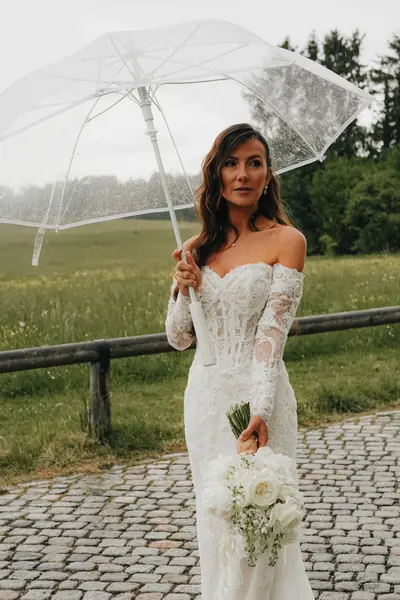 Braut mit Regenschirm und Spitzenkleid im Regen