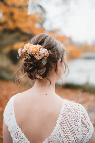 Hochgesteckte Brautfrisur mit Blüten im Haar und Spitzenkleid