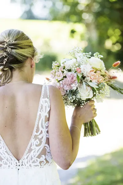 Tief gesteckte Brautfrisur und rückenfreies Spitzenkleid mit Brautstrauß